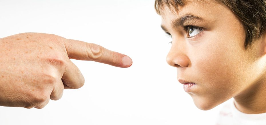A photograph of a little boy being disciplined.  An angry child stares back in anger and defiance as he is being disciplined.  The finger of an adult is pointing directly at him.